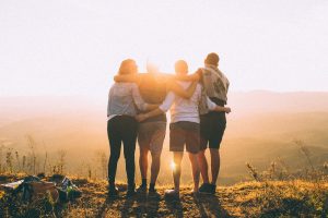 A photo of four people facing a sunset, holding each other.