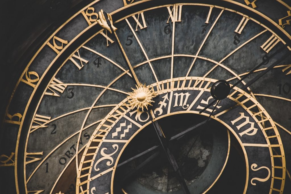 A clock with roman numerals and astrological symbols.