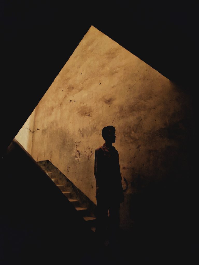Image of a person descending a staircase from a lit background into darkness.